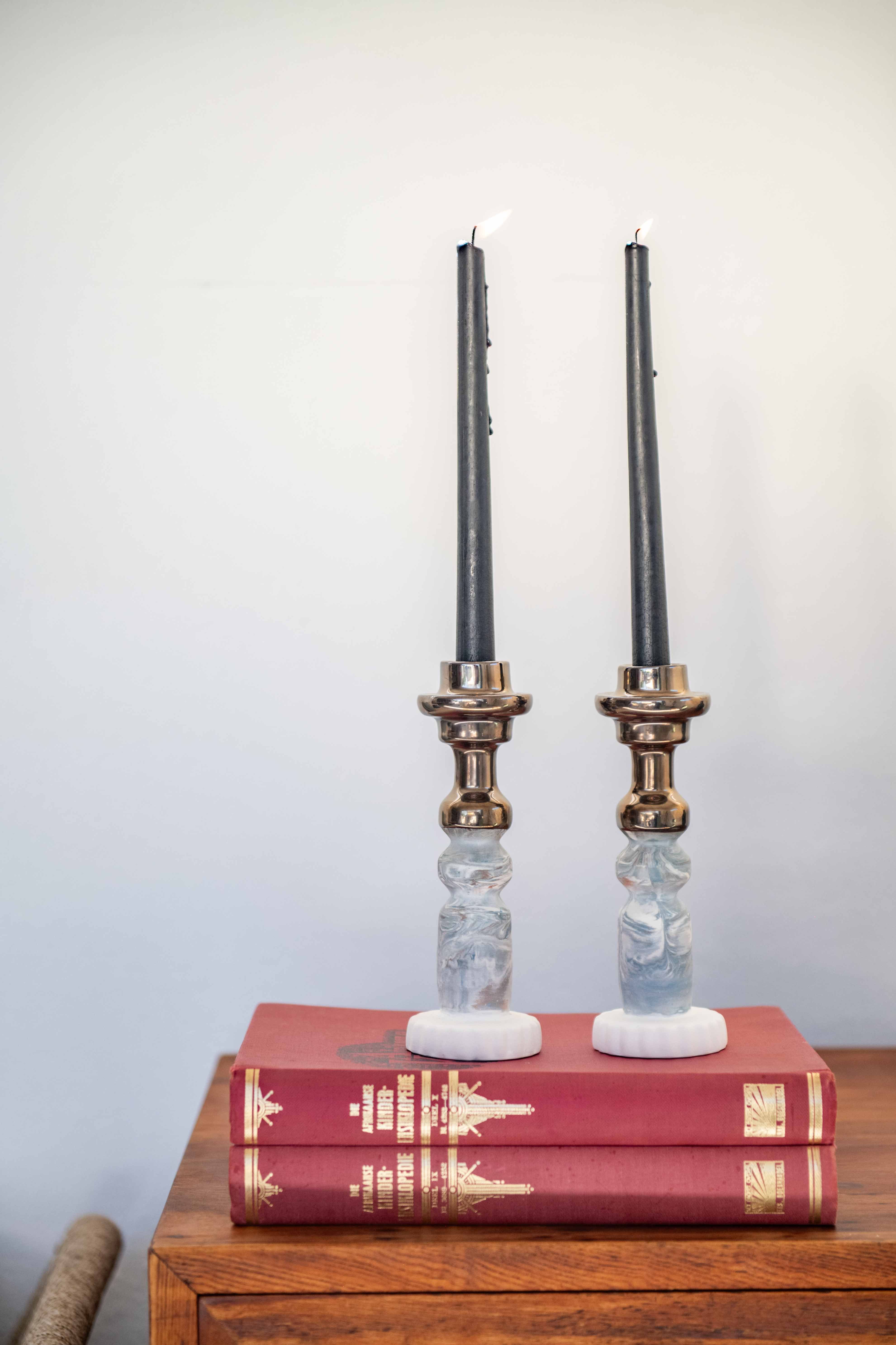 two Rialheim Candle stick holders with blue and white clay and bronze tops on red books with a white back ground