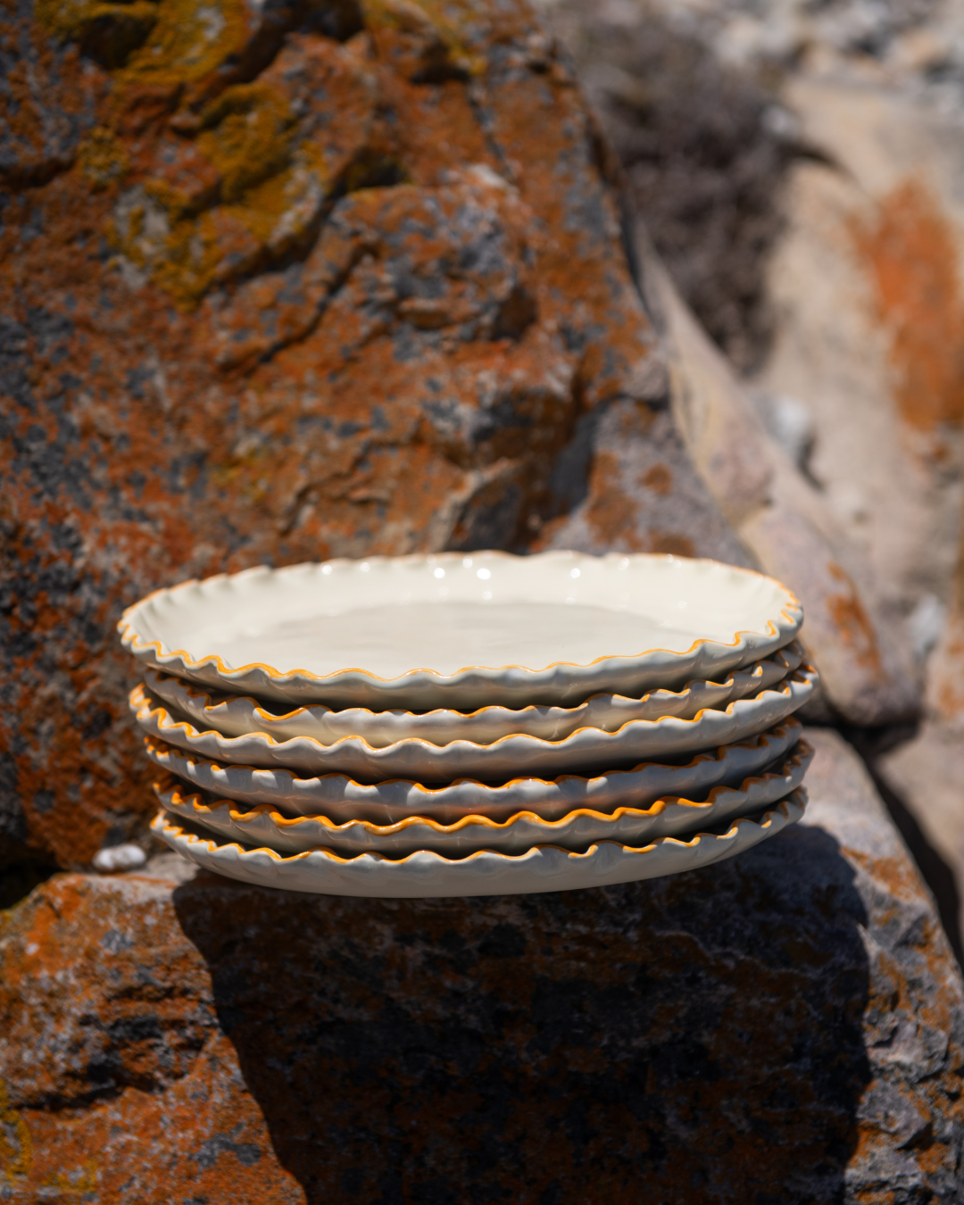 Stack of ceramic plates with scalloped edges on a textured stone surface