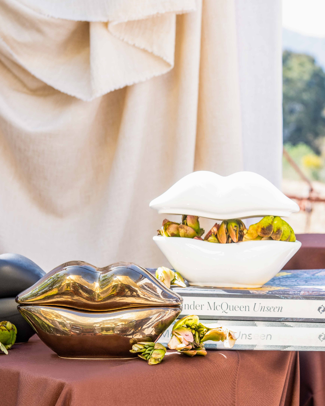 Decorative gold lip-shaped object on a table with a white bowl containing food and books in the background.