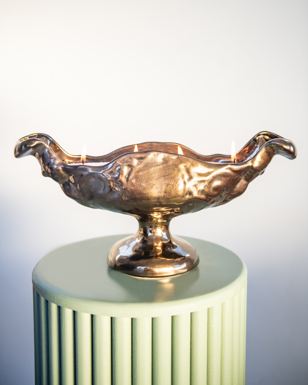 Bronze bird-shaped object on a cylindrical green stand against a light gray background