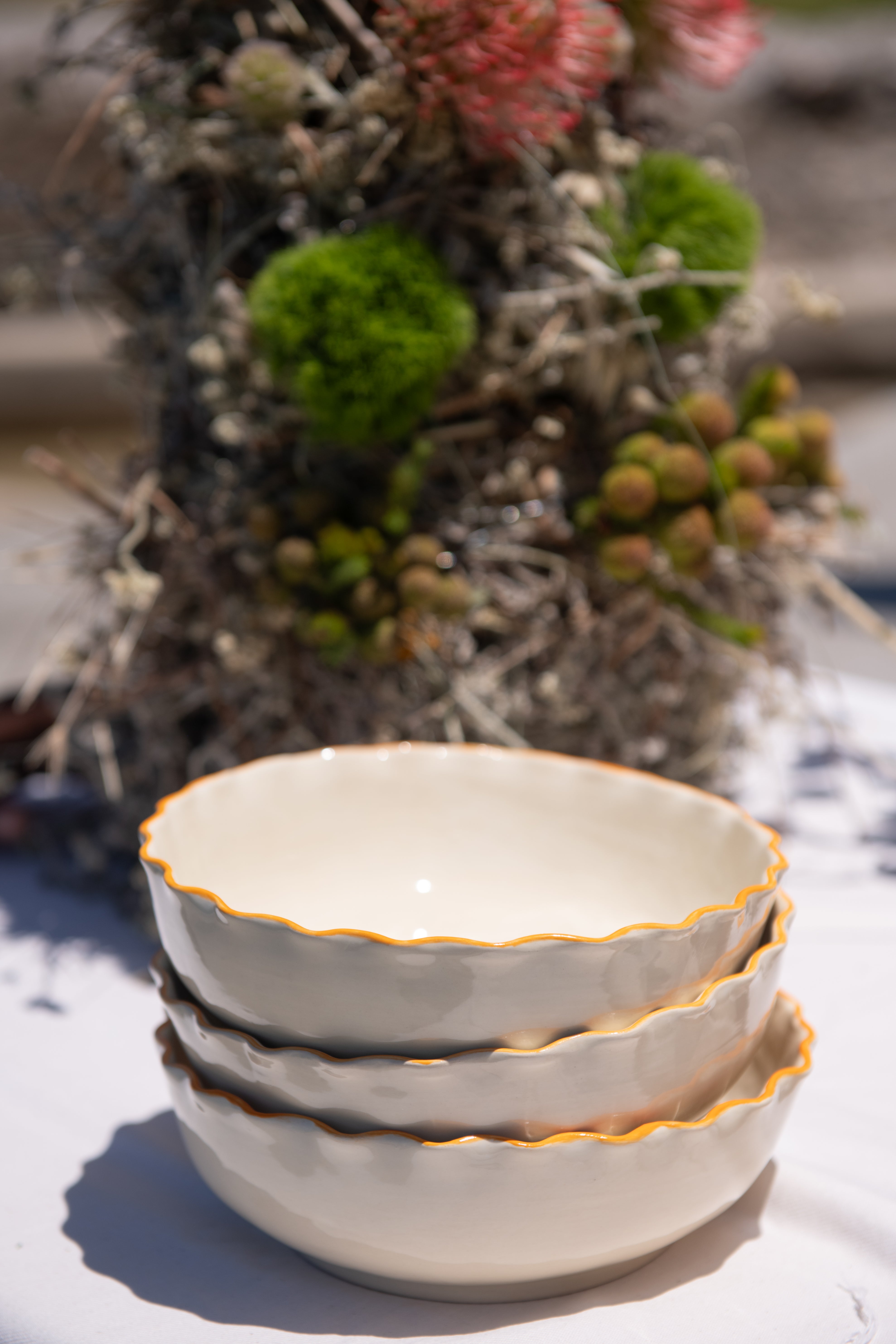 Stack of ceramic bowls with coral rims on a white surface with plants in the background