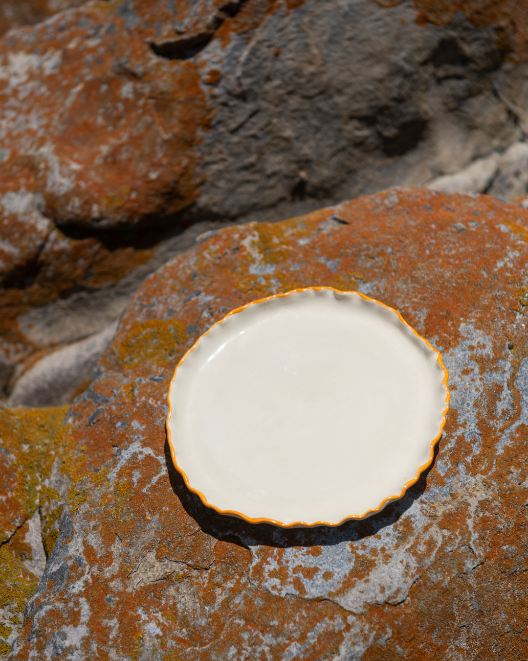 Round ceramic side plate coral rim on a textured brown surface