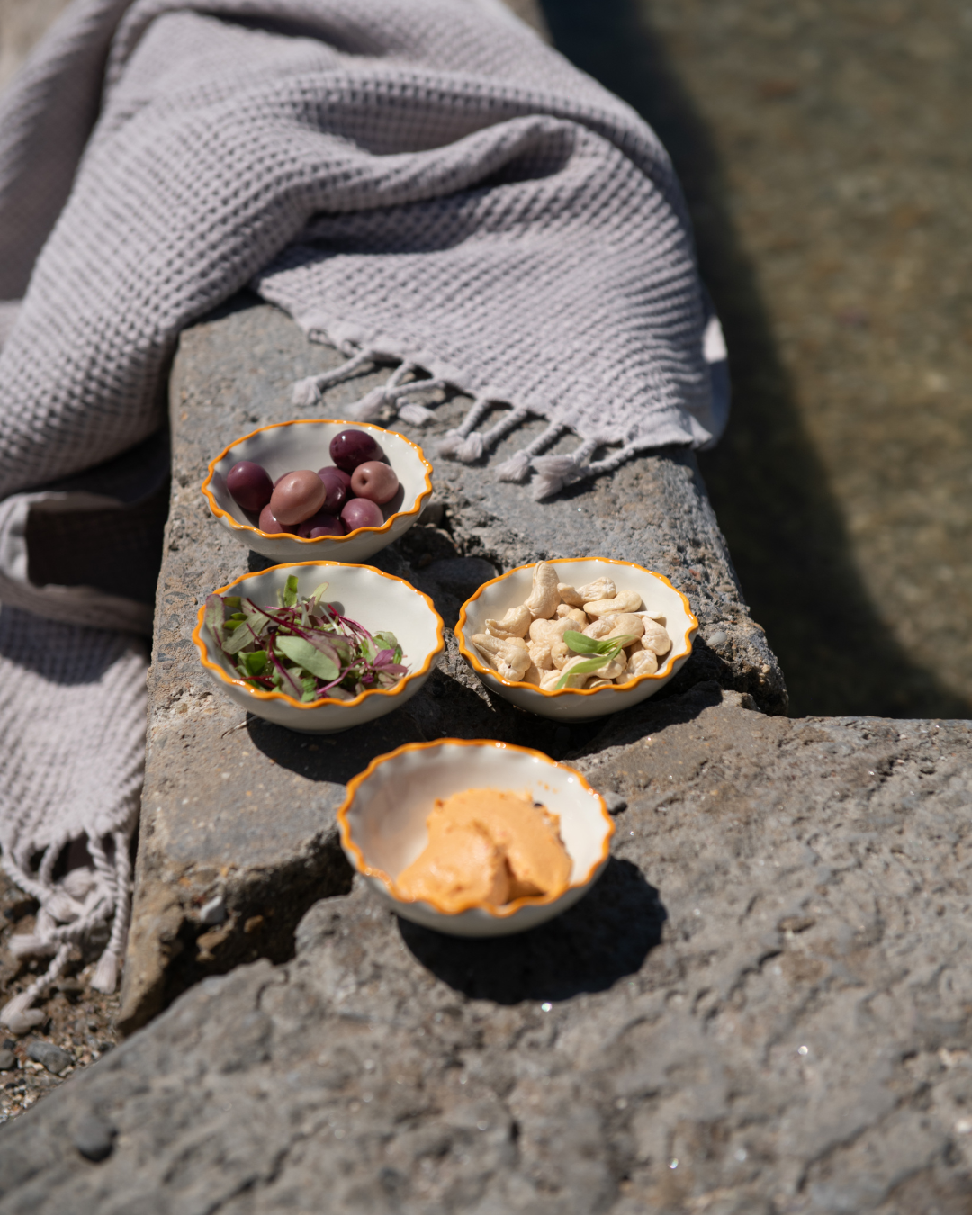 Four small bowls with food on a stone surface with a gray towel.