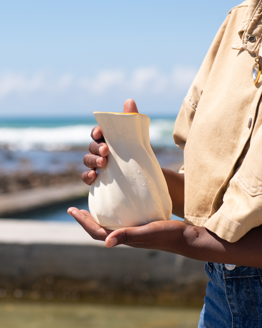 Person holding a white shell  jug by the ocean