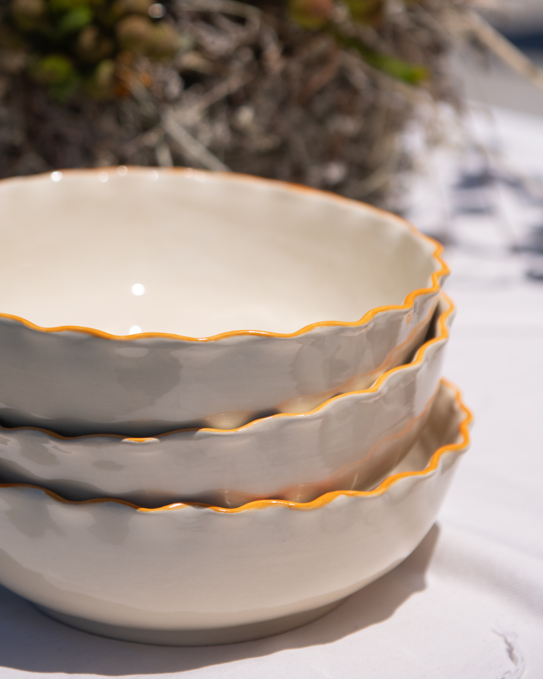 Stack of ceramic bowls with coral rims on a light surface.
