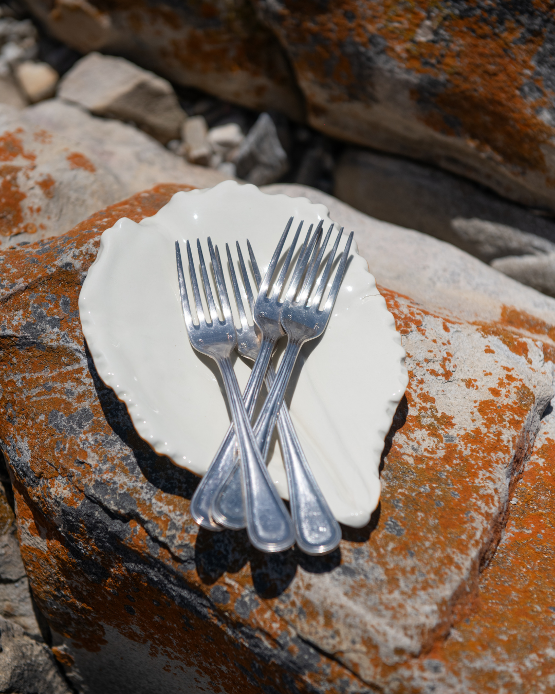 Set of silver forks on a white plate with a natural stone background