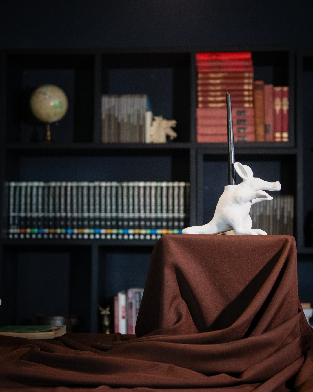 White Aardvark candle holder on a brown cloth with a bookshelf in the background