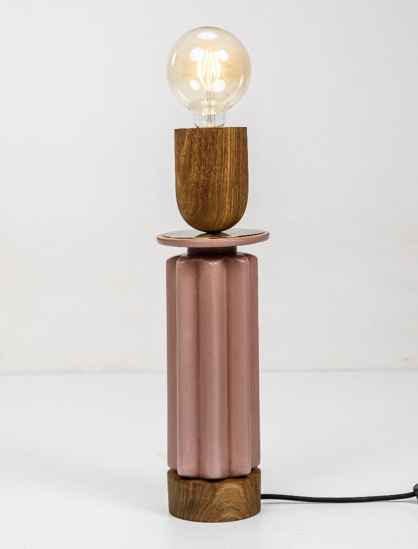 A Scallop Table Lamp with a blush pink scalloped base and copper details, with a light bulb on top.