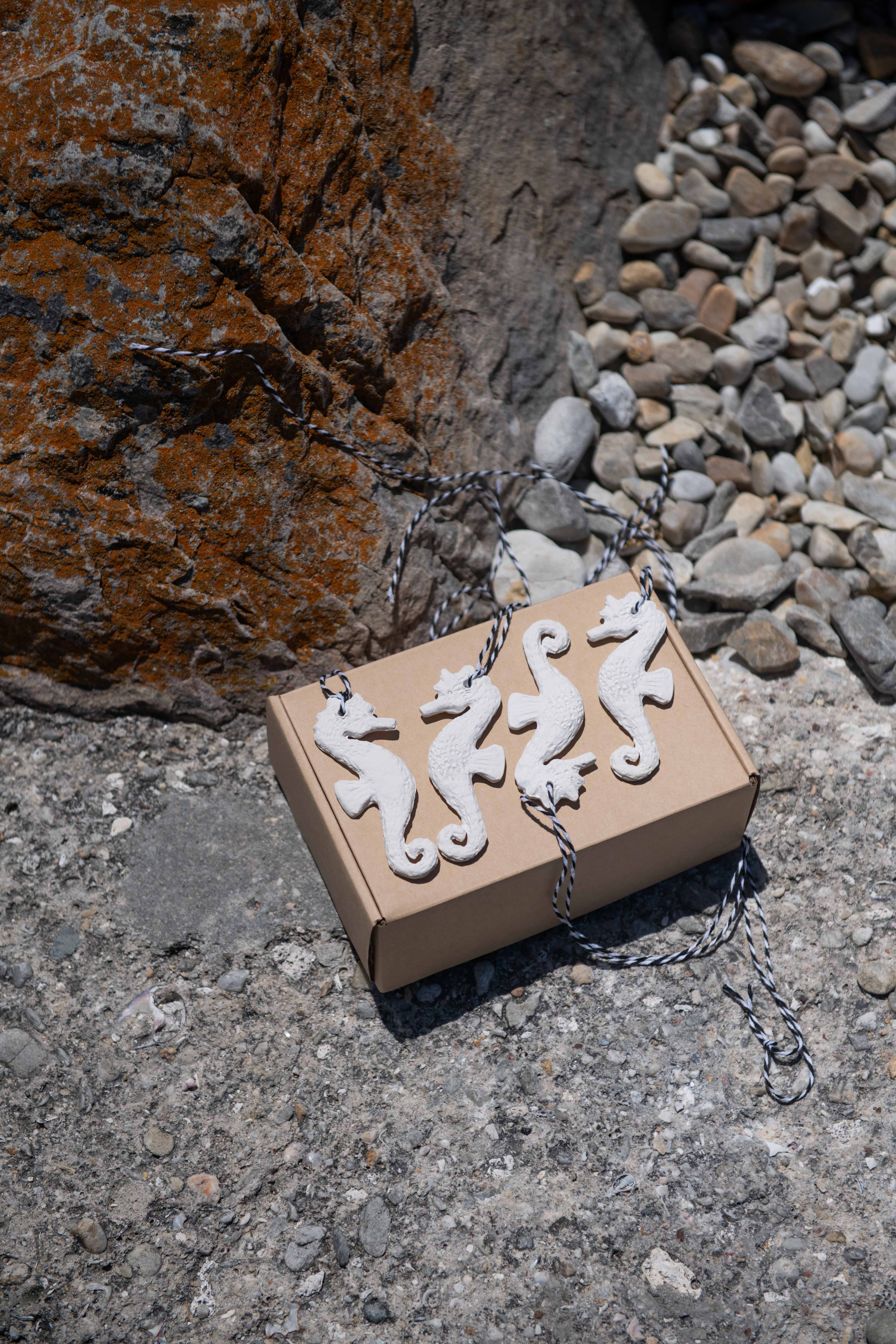 Three white ceramic seahorse figurines on a cardboard box with a natural stone background