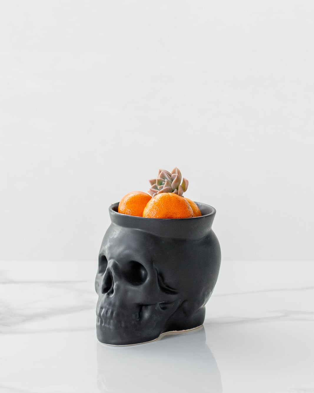 Black skull-shaped vase with oranges on a white background