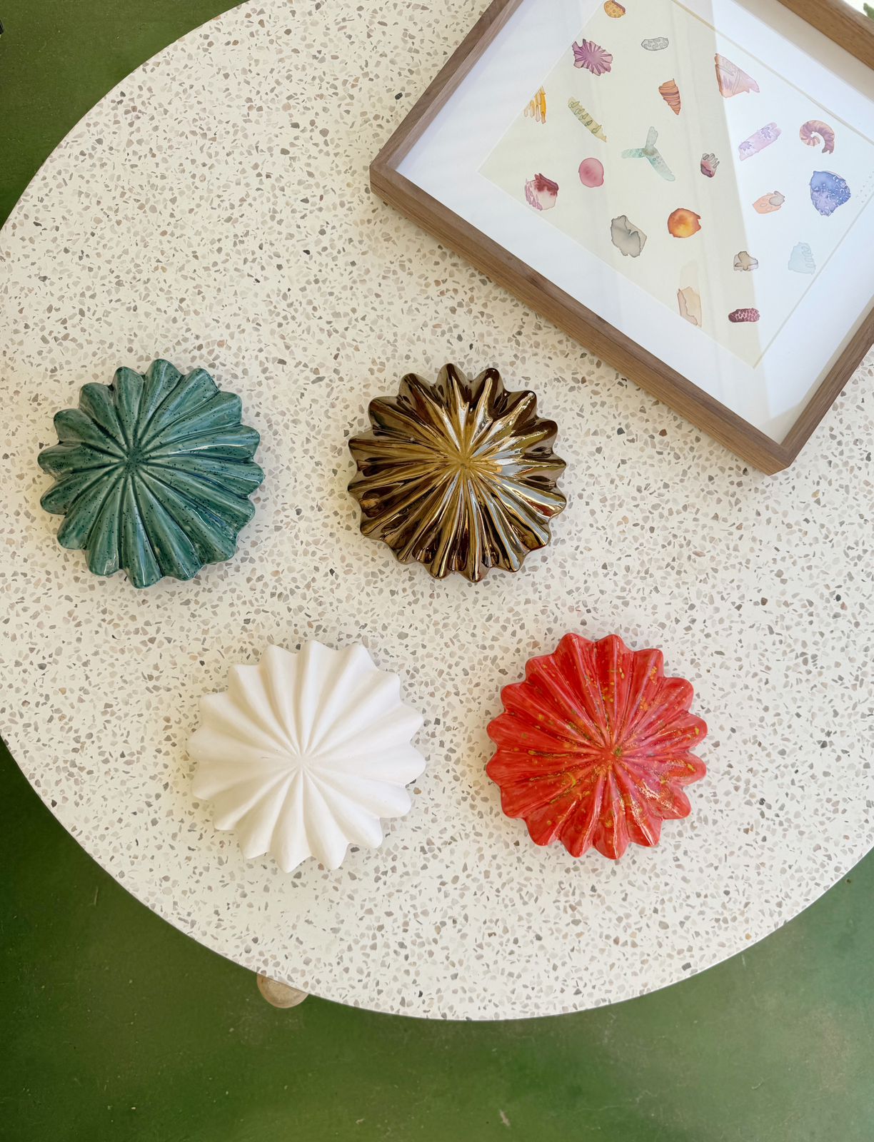 Four colorful ceramic wall art pieces on a textured surface with a framed picture in the background.