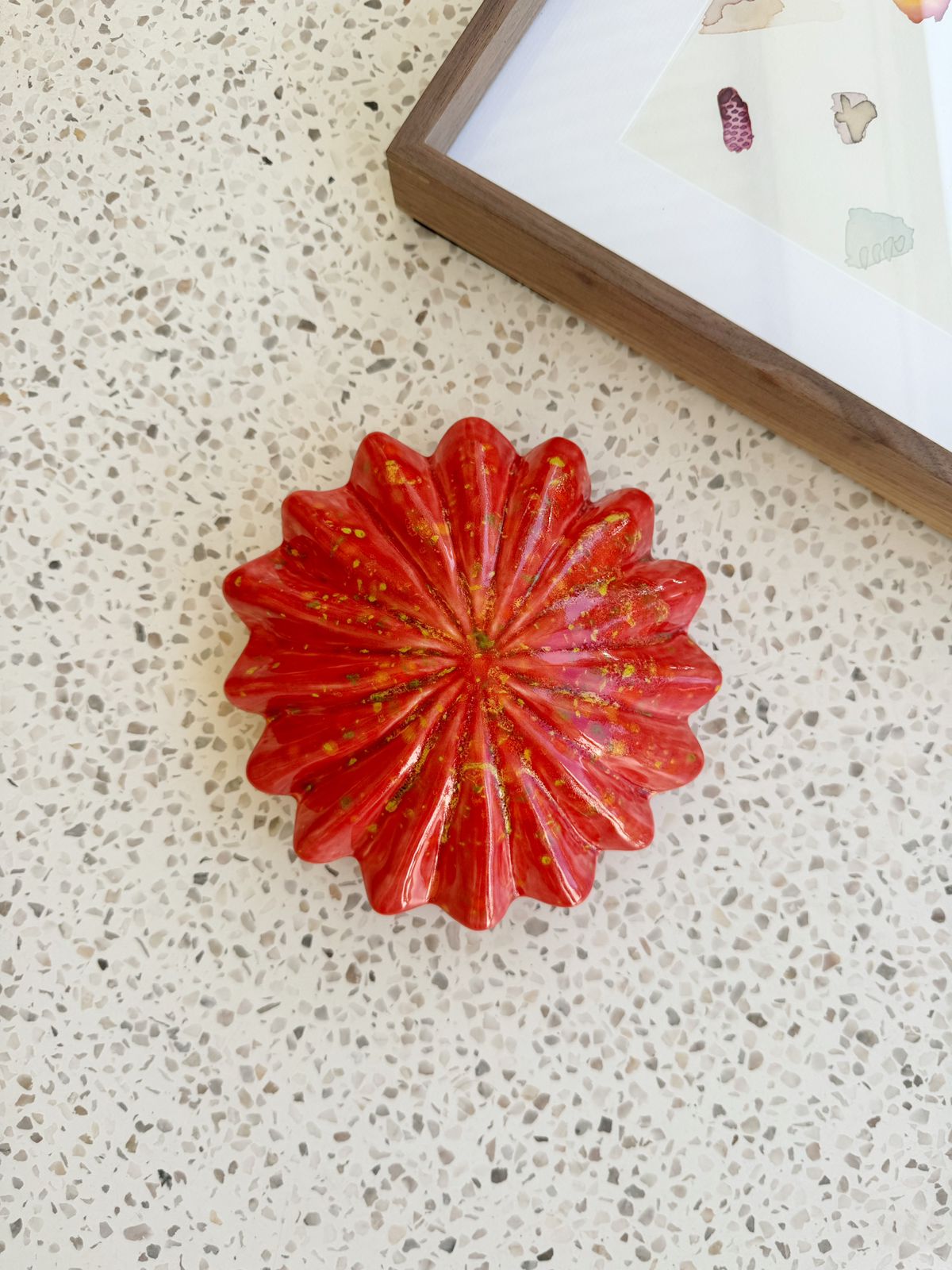 Red decorative item on a textured surface with a framed picture in the background