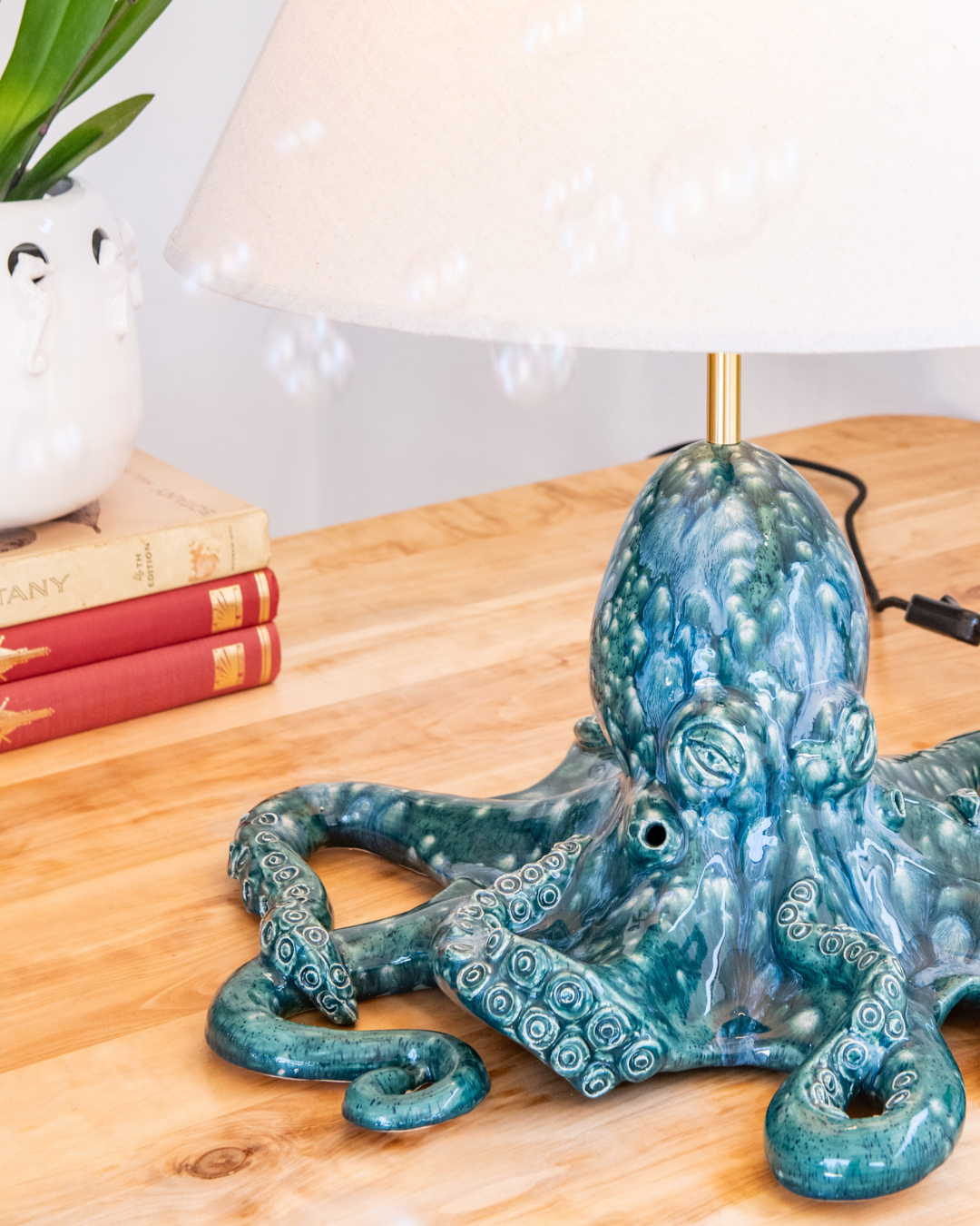 Blue octopus-shaped lamp on a wooden surface with books and a plant in the background.