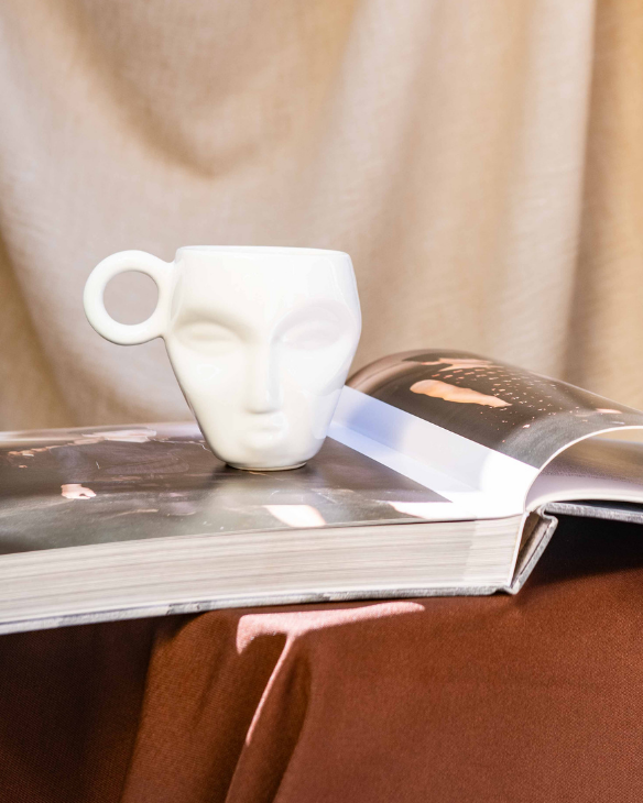 Café cup and magazine on a table with a draped curtain and outdoor view.