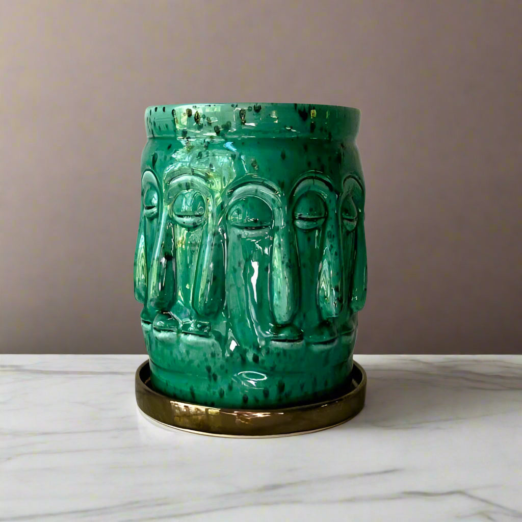 Rialheim Ceramic green planter in emerald with a bronze tray the planter has faces around it and is African in feeling