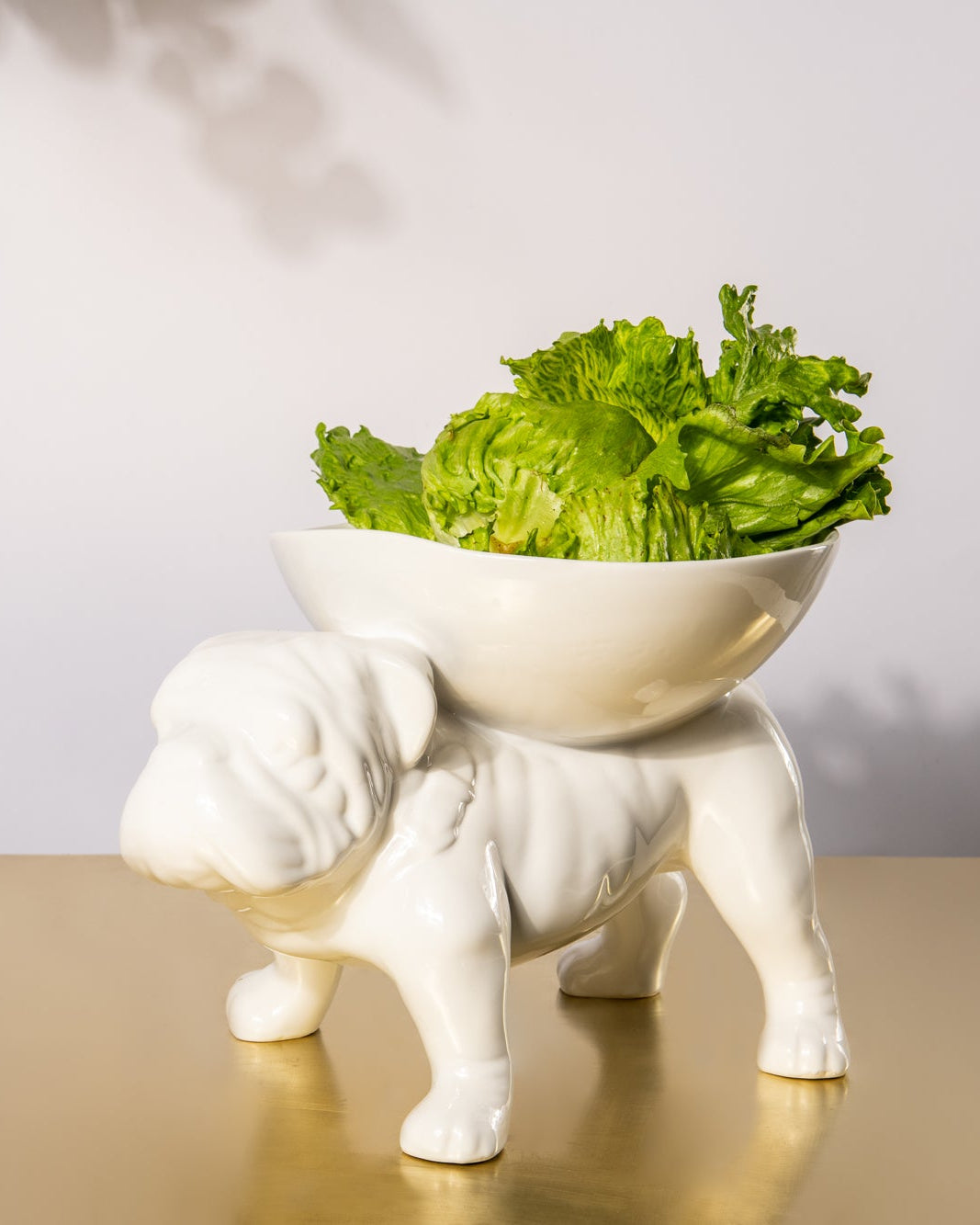 White ceramic bulldog figurine with a bowl of green salad on a reflective surface.