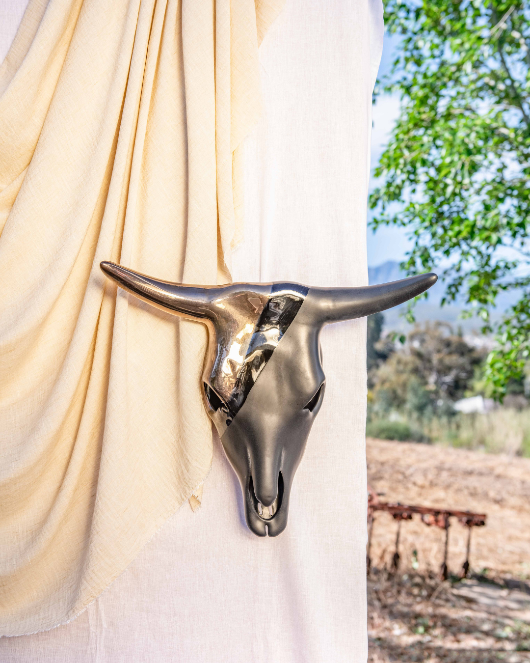 Decorative bull head sculpture against a white curtain with outdoor scenery in the background
