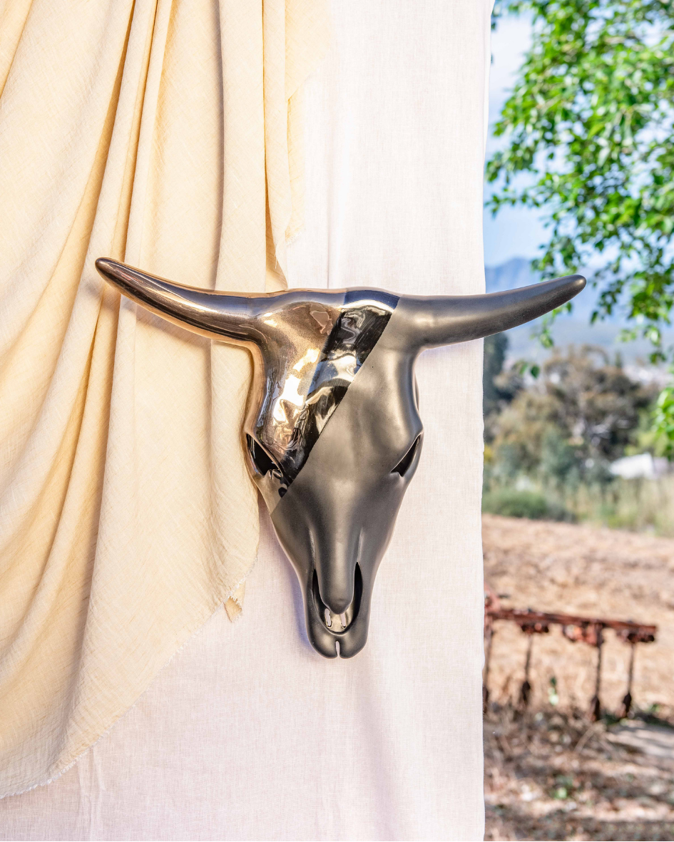 Decorative bull head sculpture against a white curtain with outdoor scenery in the background