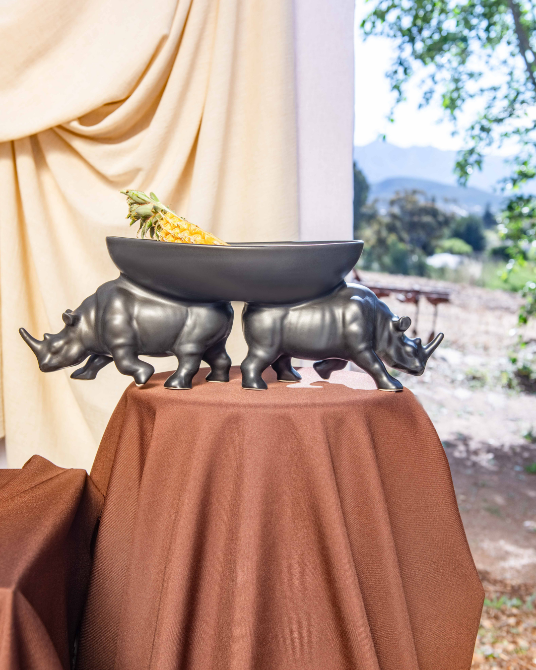 Decorative bowl with rhinoceros sculptures on a table outdoors.